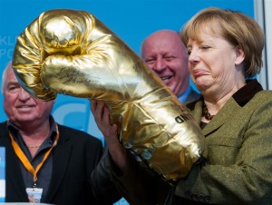 Angela Merkel egy aranyszínű óriás bokszkesztyűvel. Angela Merkel egy aranyszínű óriás bokszkesztyűvel. Forrás: or-argent.eu, Conclude Zrt.